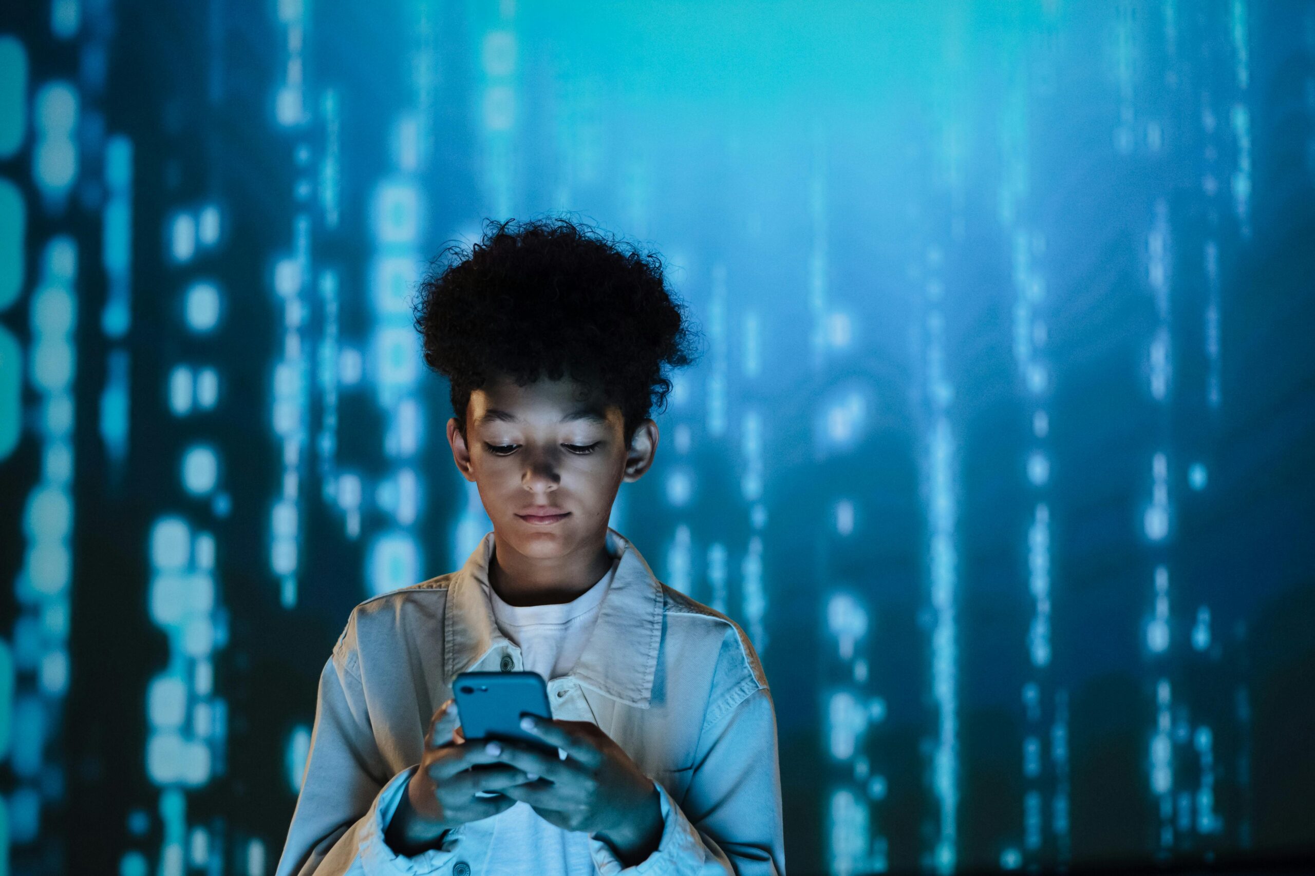 Curly-haired boy focused on smartphone amidst digital backdrop